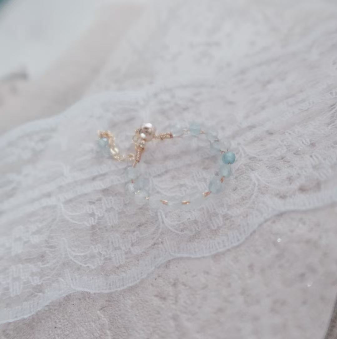 Delicate Aquamarine Faceted Bead Ring with Gold Accents on a Lace Background