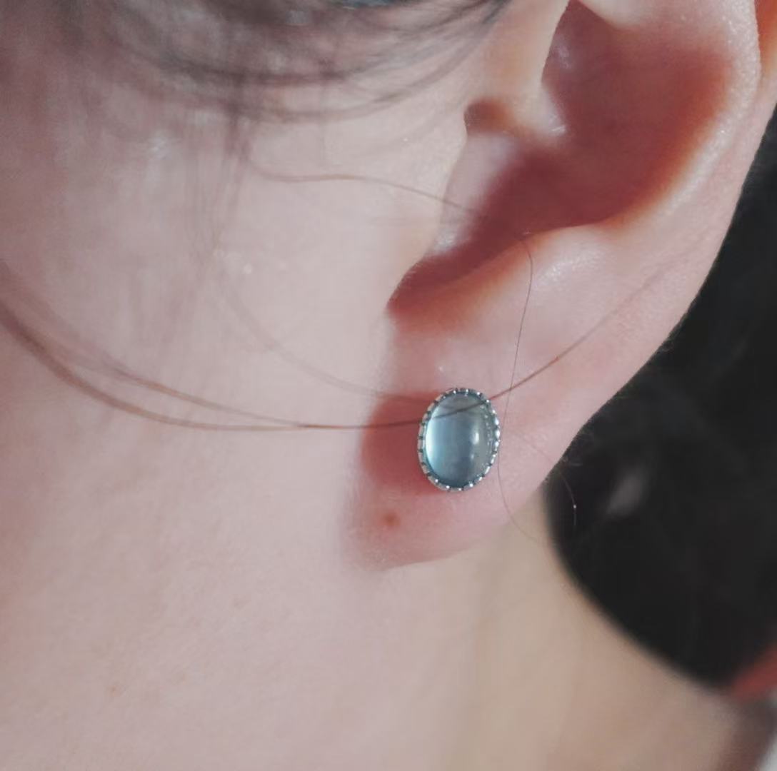 Elegant Aquamarine Oval Stud Earrings set against a model's ear, showcasing their unique design
