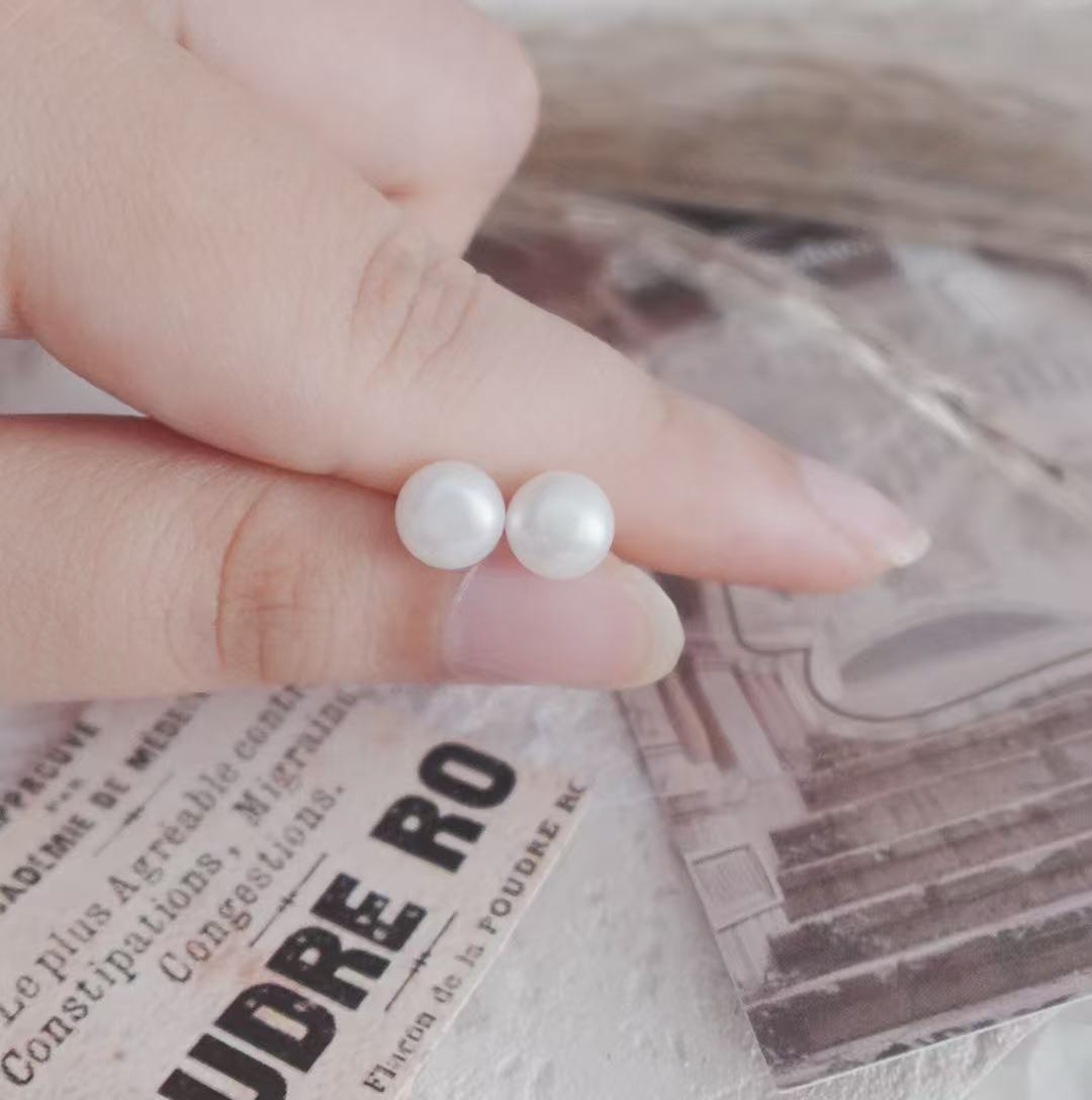 Natural Freshwater Pearl Oval Stud Earrings held between fingers against a vintage background