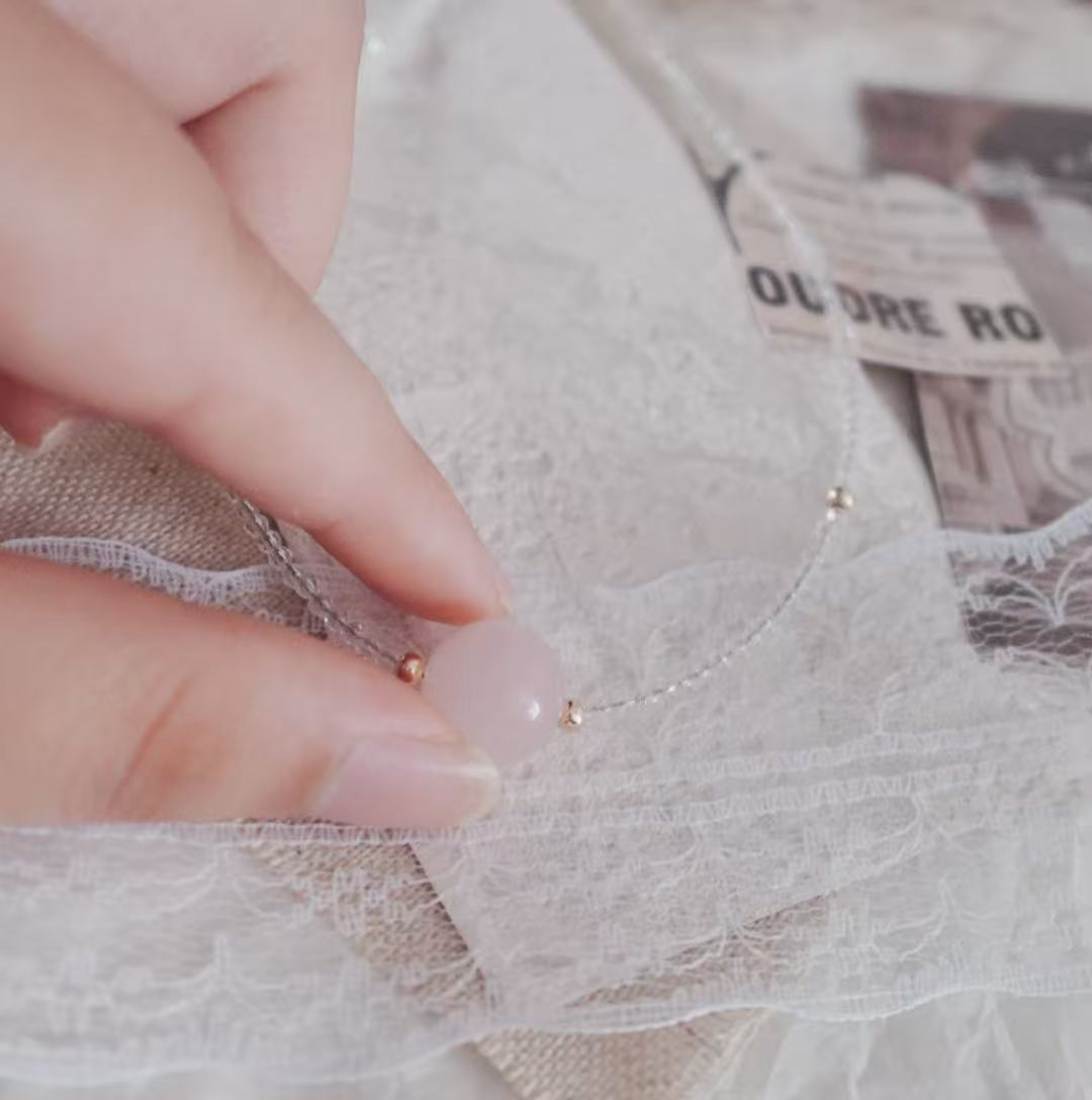 Hand showing a Rose Quartz Beaded Necklace on soft lace fabric for a delicate touch