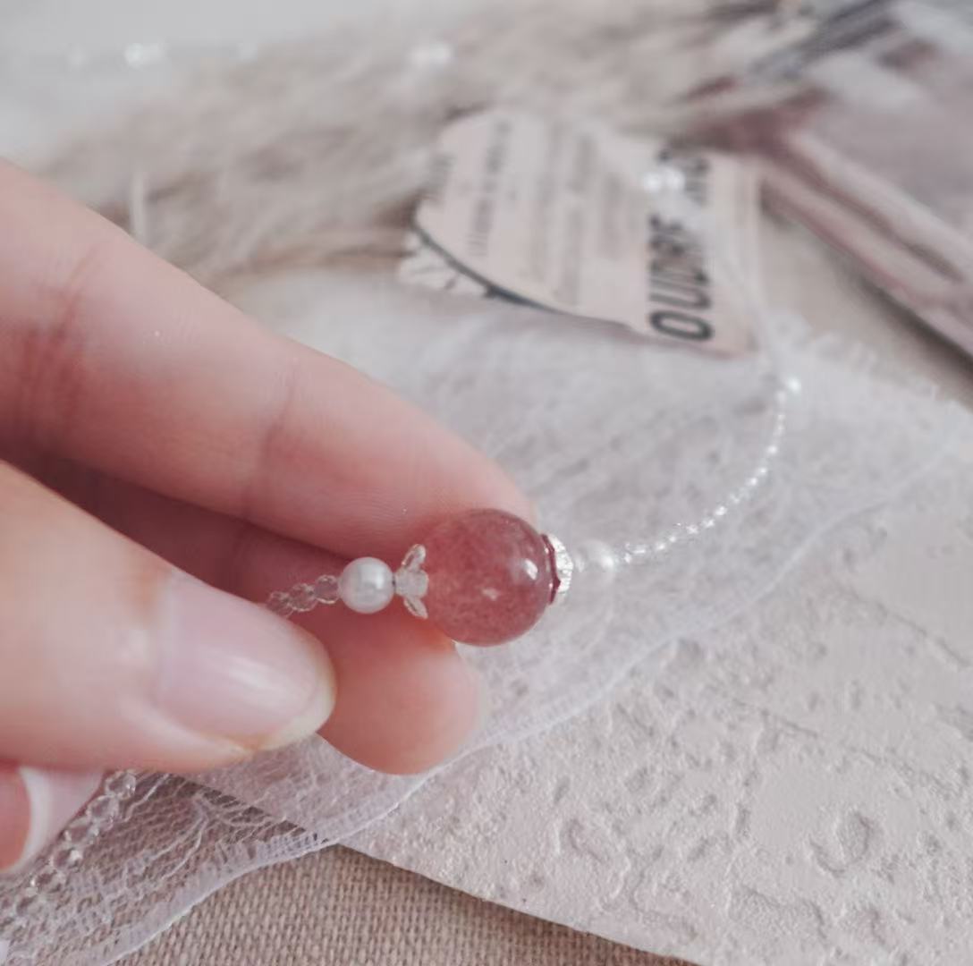 Close-up of a Strawberry Quartz Beaded Necklace held in hand showcasing its shimmering beads