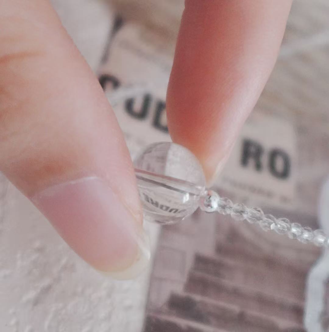Close-up of a White Crystal Beaded Necklace showing a clear bead being held between fingers